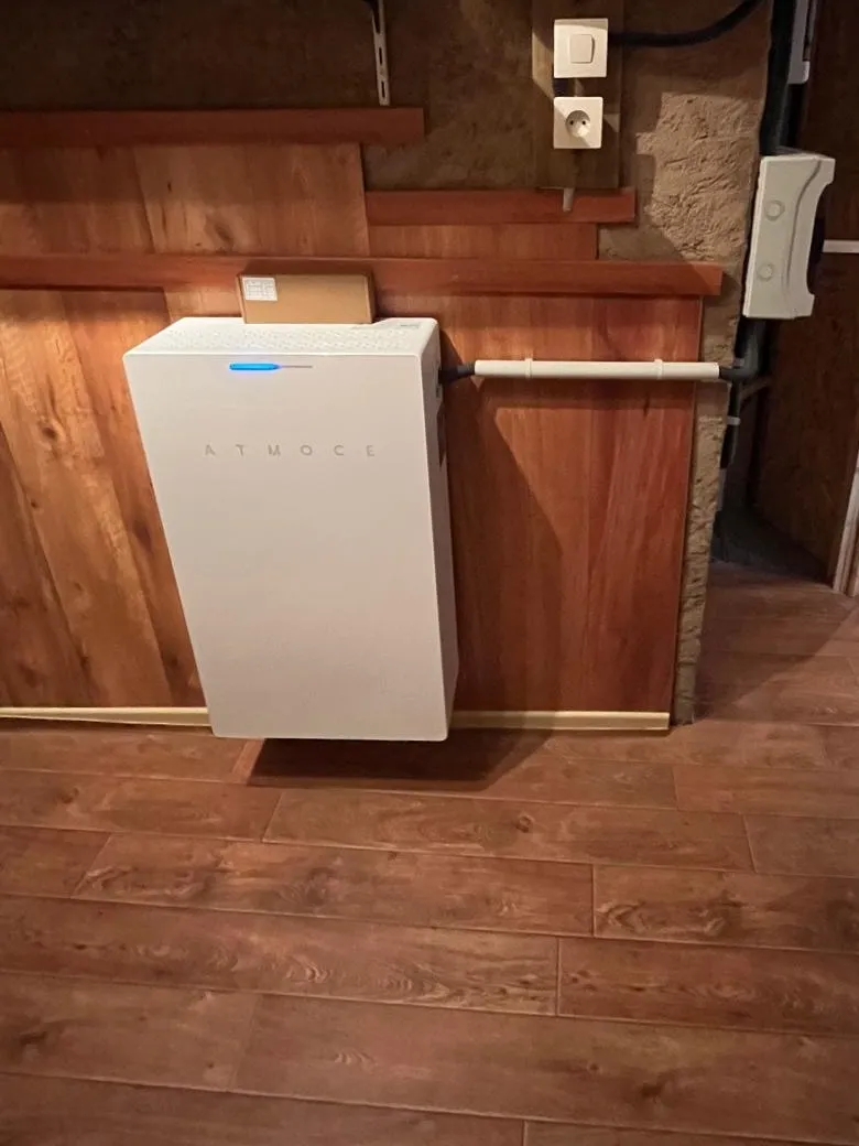 Batterie de stockage Atmoce installée par ISL CLIM contre un lambris, à côté du tableau électrique