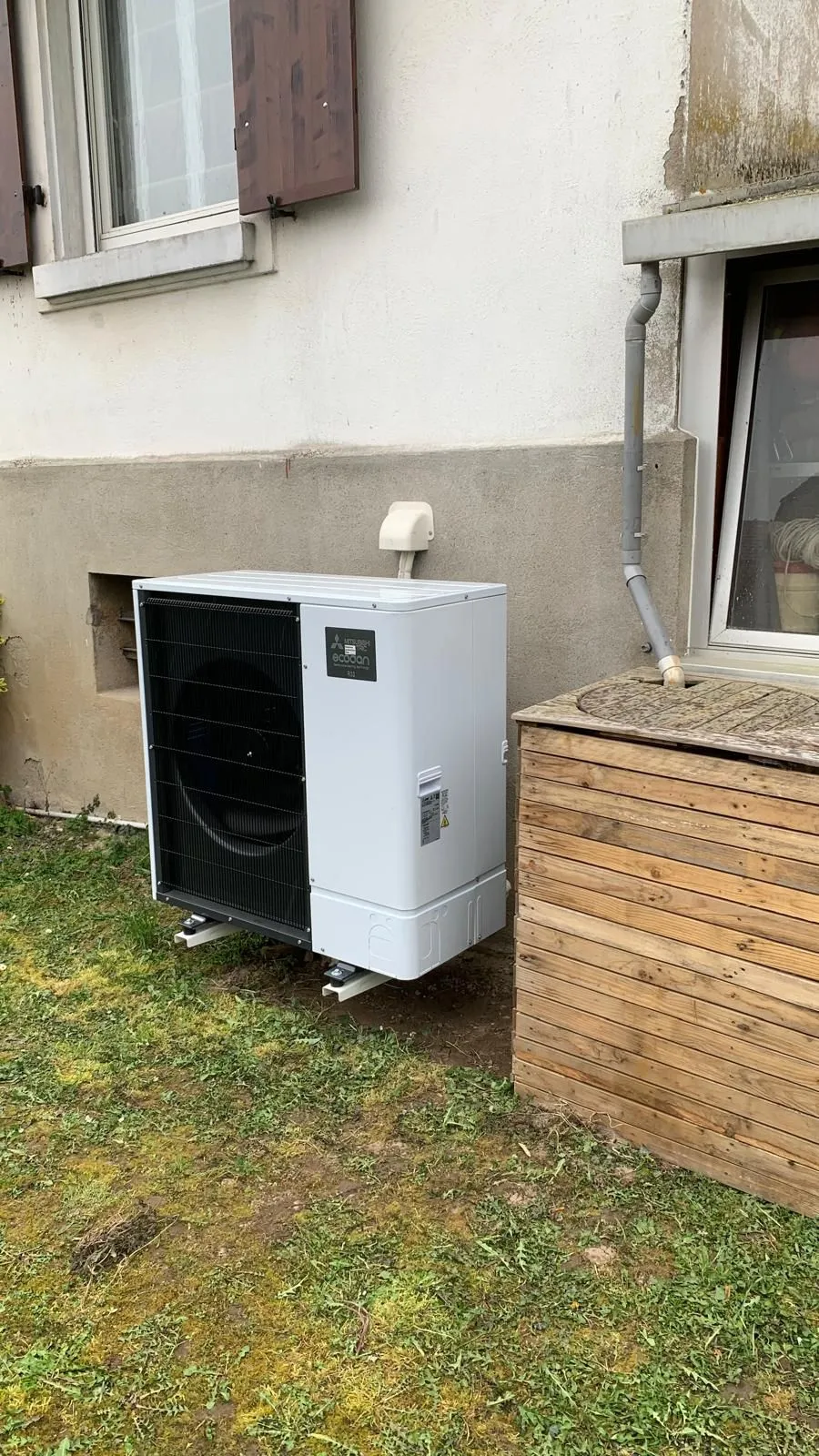 Unité extérieure de pompe à chaleur air/eau Mitsubishi Electric Ecodan posée sur socle dans un jardin, installation ISL CLIM