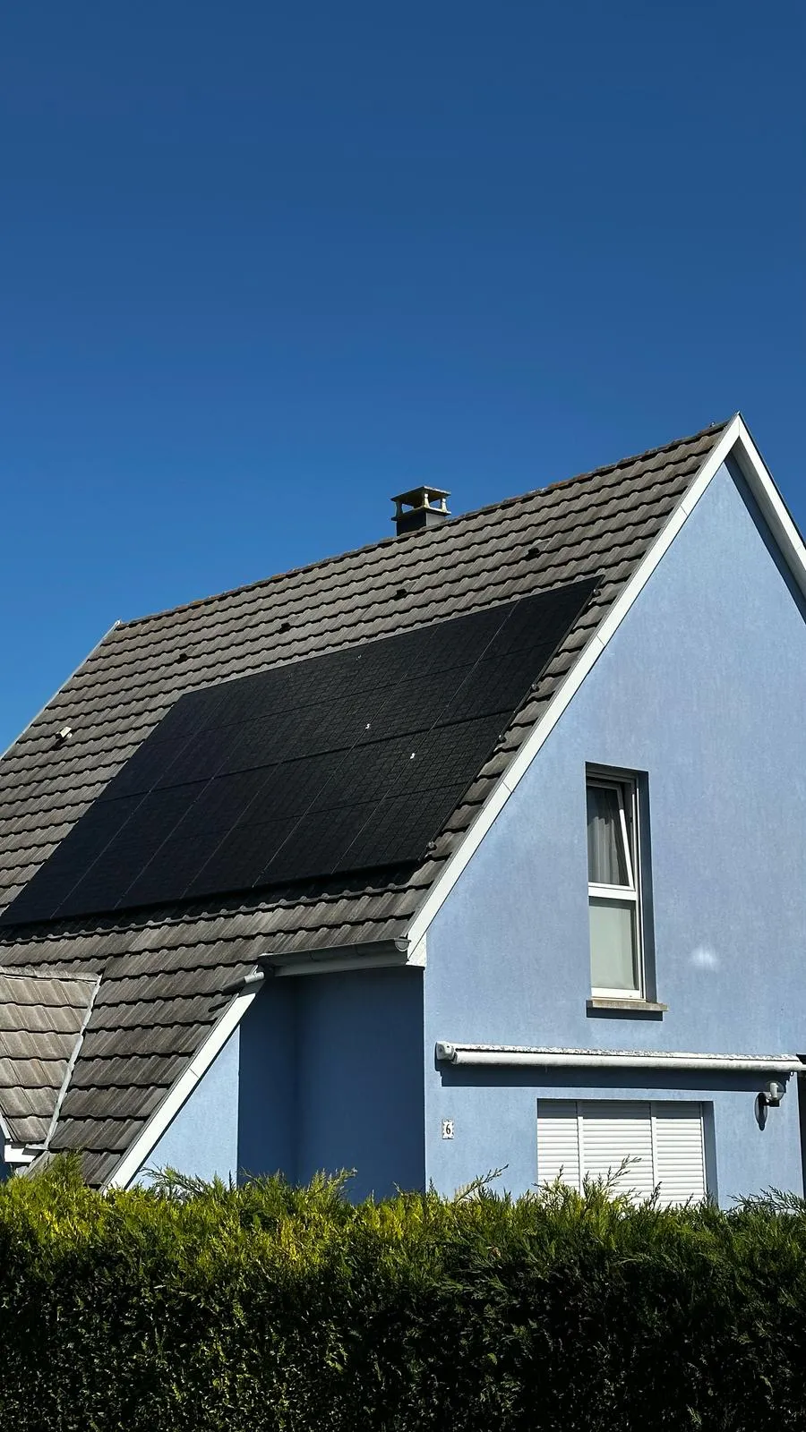 Panneaux photovoltaïques noirs posés par ISL CLIM sur la toiture en tuiles d’une maison à façade bleue en Alsace