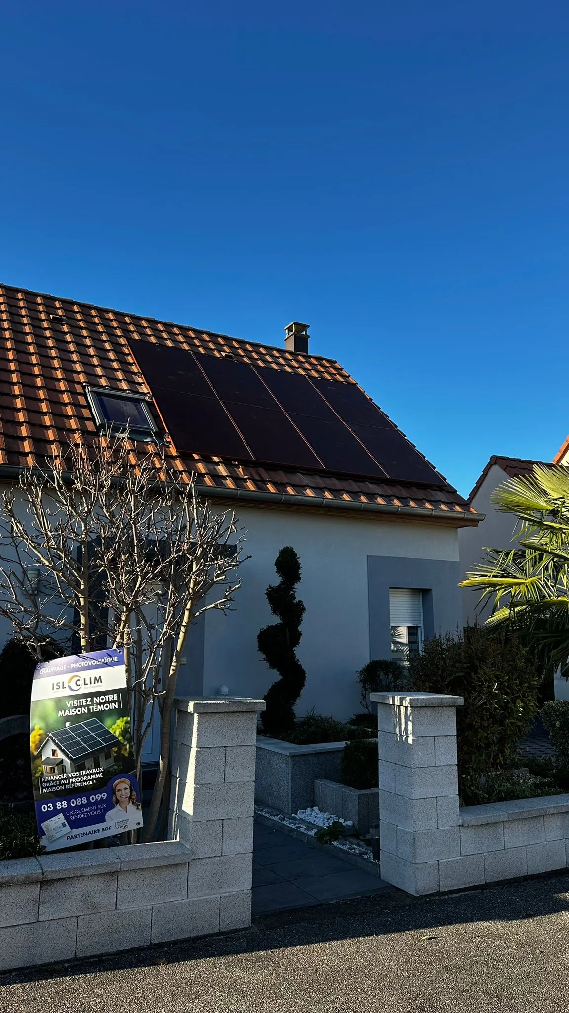Maison témoin ISL CLIM équipée de panneaux photovoltaïques, avec panneau d’information devant le portail
