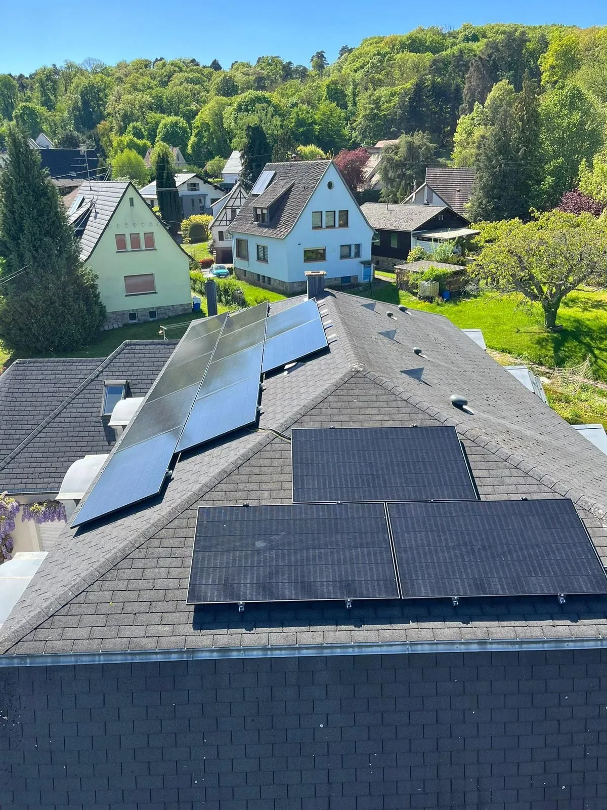 Panneaux photovoltaïques noirs installés par ISL CLIM sur une toiture en bardeaux, sous un ciel dégagé, dans un village en lisière de forêt