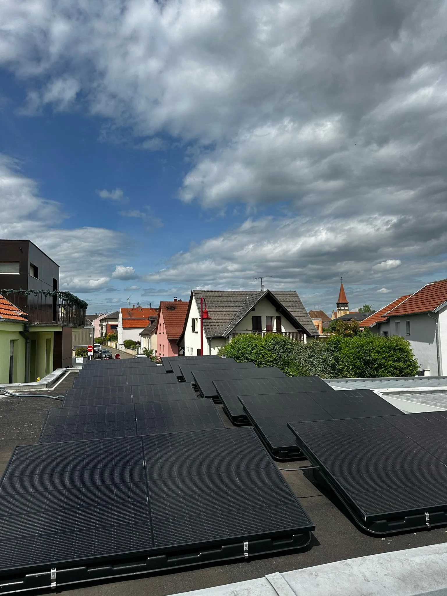 Rangées de panneaux photovoltaïques noirs installés par ISL CLIM sur une toiture-terrasse dans un village alsacien