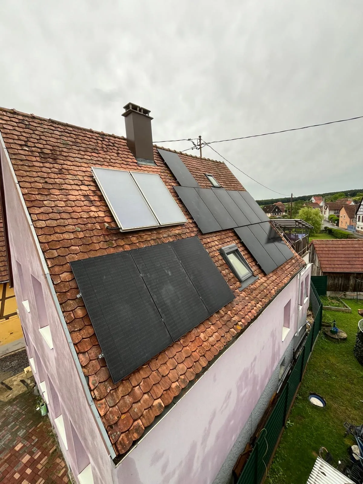 Panneaux photovoltaïques installés par ISL CLIM sur une toiture en tuiles anciennes, à côté de deux capteurs solaires thermiques