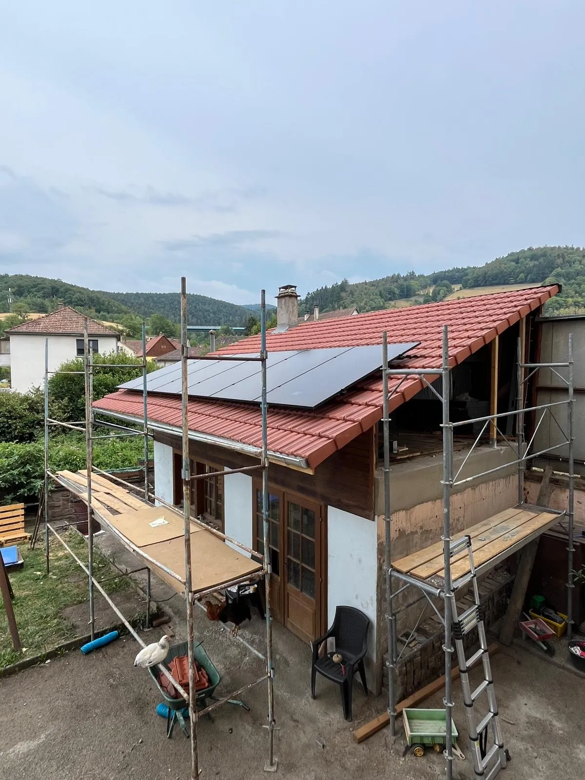 Panneaux photovoltaïques posés par ISL CLIM sur une toiture en tuiles rouges, échafaudage encore en place, dans une vallée boisée